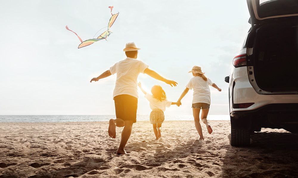 AdobeStock_548534936_ext family flying kite on beach next to SUV